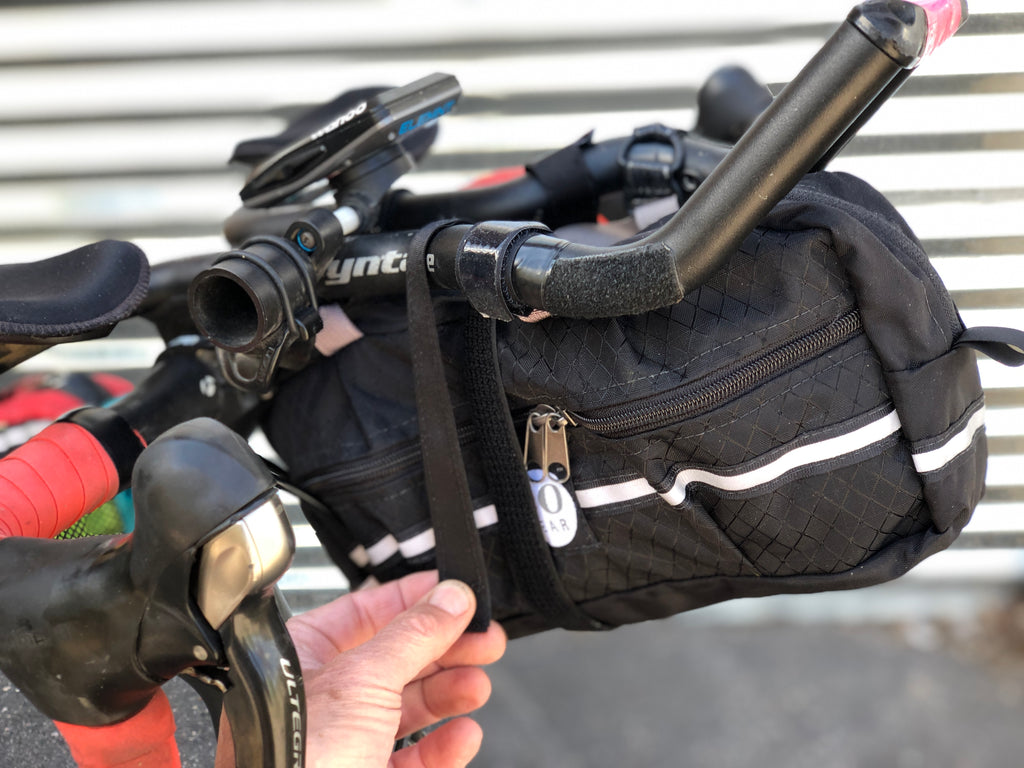For heavier loads (i.e. full water bottle) the provided D-ring compression strap helps prevent sway. INSTRUCTIONS: Loop it through itself on the opposite side and bring it underneath and around the other “bar.”